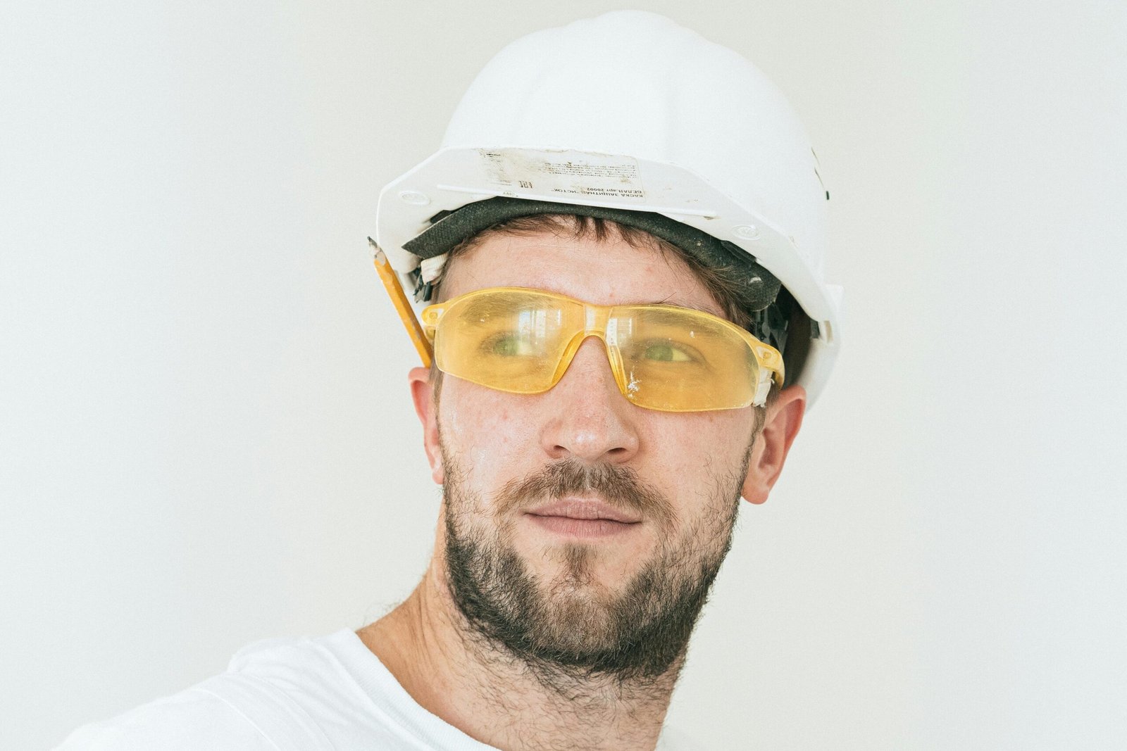 Close-up of a bearded construction worker with safety goggles and hard hat on white background.